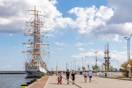 Tourists walk around the marina near sailing ship Dar Mlodziezy (Gdynia, Polan ...