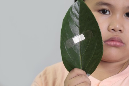 Environment conservation concept - boy holding a leaf with bandage.の写真素材