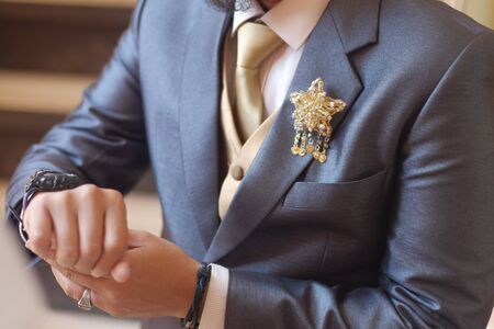 Man in dark grey suit two bottons golden star brooch, checking whatch, close upの写真素材