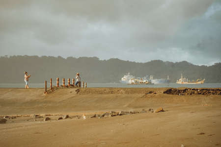 Cilacap, Indonesia - July 14 2020: sunset moment at Teluk Penyu Beach. People picnic and ship in frameのeditorial素材