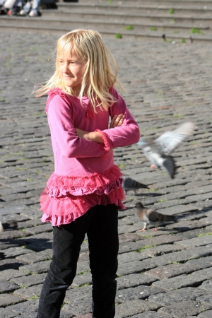 A pretty young blond girl watching pigeons fly in a park in Quito, Ecuadorの写真素材
