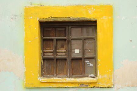 A window with wood shutters in a yellow frame in the wall of a building in Cotacachi, Ecuadorの写真素材