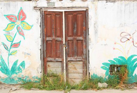 A weathered red door in a wall with a painted flower in Cotacachi Ecuadorの写真素材