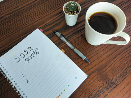 Business concept 2022 goal list with notebook, cup of coffee on a wooden table and cactus plants to decorateの写真素材