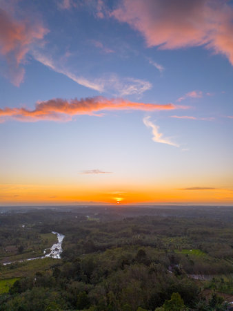 Beautiful landscape view at sunrise showing a winding river through countryside with forests and hills under a dramatic orange and blue skyの写真素材