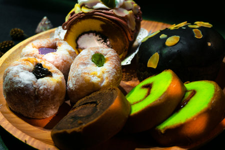 Indonesian sweet cakes served on natural wooden plate and spoon with black background highlighting traditional dessert texture and authentic tropical food styleの写真素材