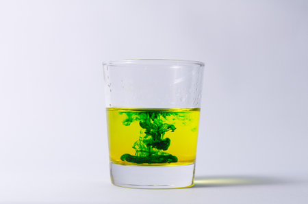 Vibrant Green Ink Swirling in Yellow Water in Glass