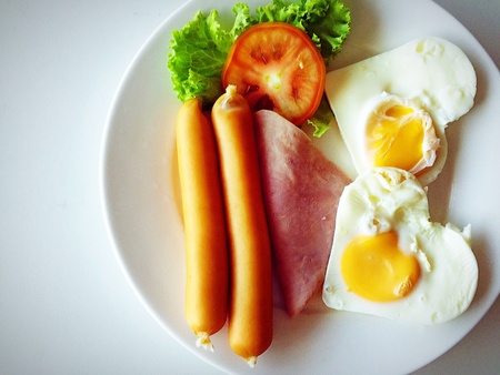 Breakfast includes heart-shaped eggs, sausages, ham, lettuce decorated with warm light,breakfast conceptの素材