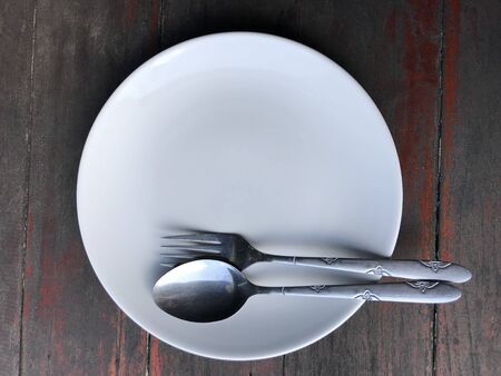 A white dish with a fork and spoon to wait to eat on the wooden floor