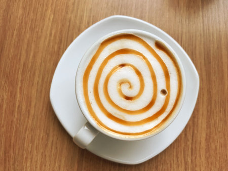 The hot caramel macchiato cup, decorated with milk foam and sprinkled with coffee powder, gives a very pleasant feeling to drink with copy spaceの写真素材