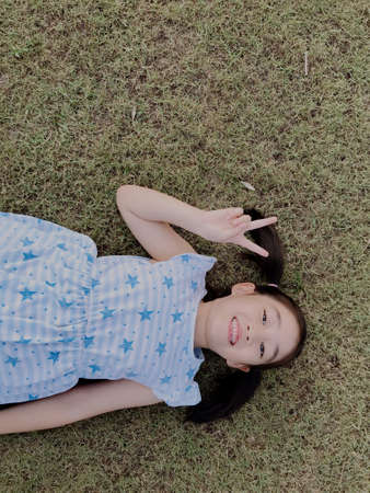 A girl tying her hair in a blue star-patterned dress lies on the grass.の写真素材