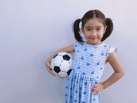 A girl with two hair tied up in a blue star-patterned outfit holding a soccer ball.の写真素材