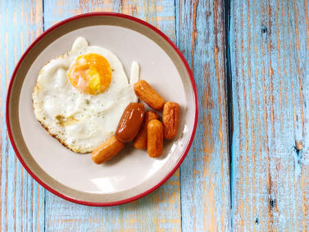 Top view of a plate of food with fried eggs and fried sausages on wooden background.