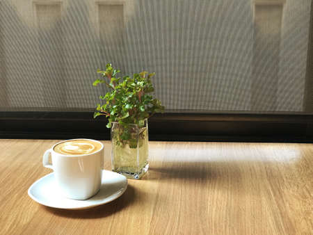 A hot latte in a white cup of coffee placed on a wooden table creates a warm morning atmosphere.