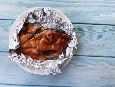 Roasted chicken is placed on foil to preserve the heat, placed on a white plate ready to eat.の写真素材