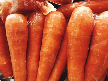 An image of orange carrots wrapped in plastic is sold at the vegetable market.