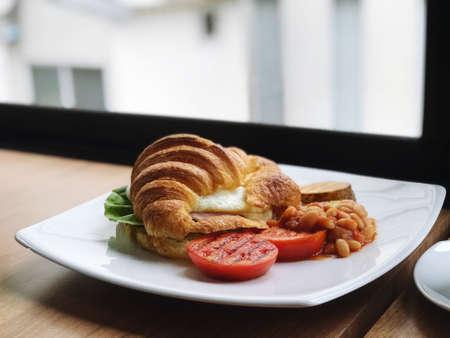 Breakfast made with eggs and croissant, laid out and decorated with red tomatoes for breakfast with hot coffee.の写真素材