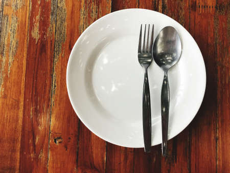 Stainless steel spoon and fork placed on a white plate ready to eat.の写真素材