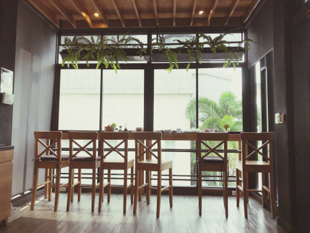 Picture of a wooden chair and table seat in a coffee shop by a large window.