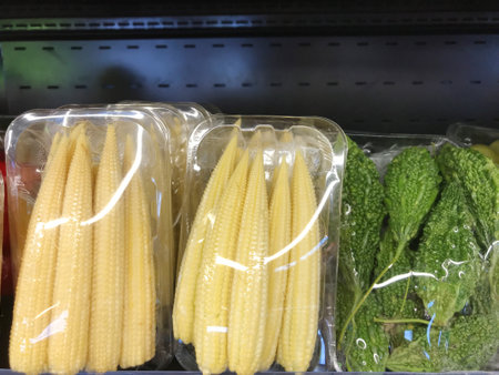 Baby corn and bitter gourd are packed in trays and wrapped in plastic and are sold in fruit and vegetable layers.の写真素材