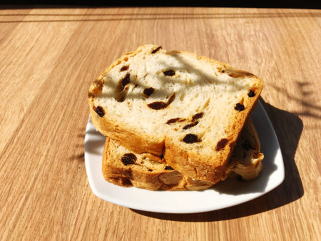 Sliced bread with raisins on white plate placed on wooden table in minimalist cafeの写真素材