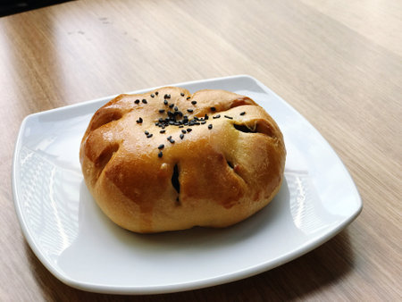 Buns filled with red bean paste topped with black sesame seeds are placed on a white plate on a...