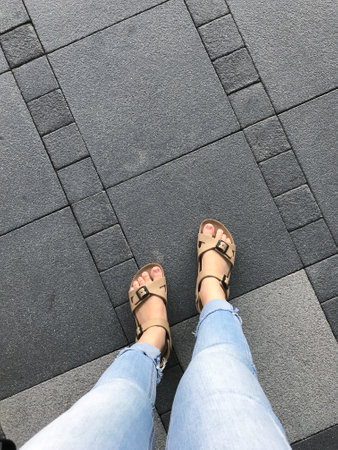 Selfie of female feet in sandals and jeans on the pavement