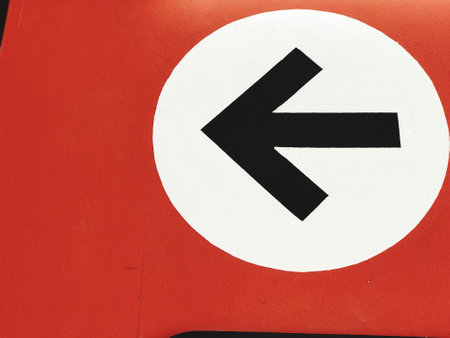 Arrow sign in red and black on white background, closeup of photo