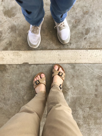 Selfie of woman and man feet in sandals on concrete floor