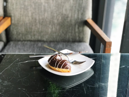 Chocolate donut on white plate with spoon on black marble tableの写真素材