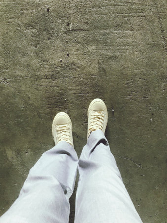 Selfie of woman's legs in white sneakers on the concrete floorの写真素材