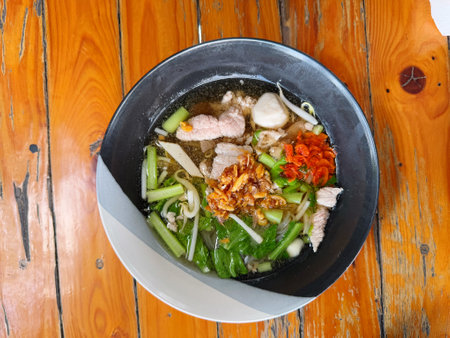 Noodles with vegetables and pork in black bowl on wooden table