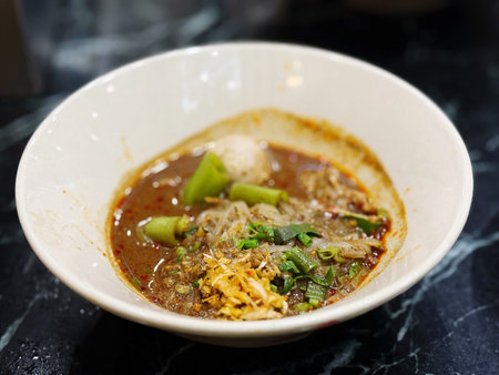 Thai spicy noodle soup with pork in white bowl on table
