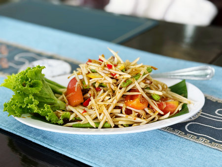 Spicy papaya salad with fresh vegetable in white plate on tableの写真素材