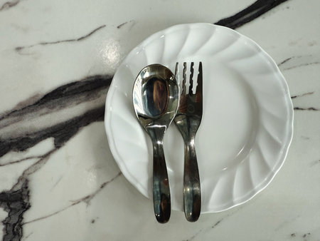 Spoon and fork on a white plate with a marble background.の写真素材