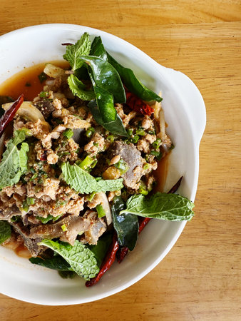 Spicy minced pork salad with basil leaf on wooden table