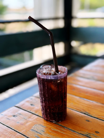 A glass of iced cola with straw on wooden table.の写真素材