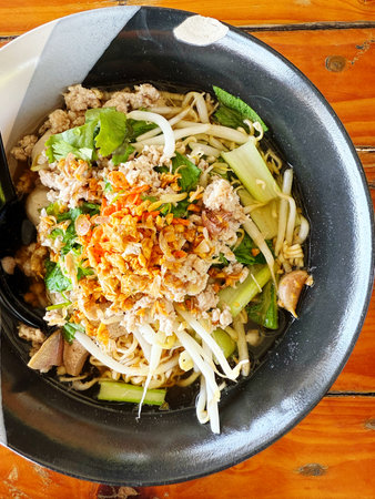 Thai spicy noodle with pork in black bowl on wooden table