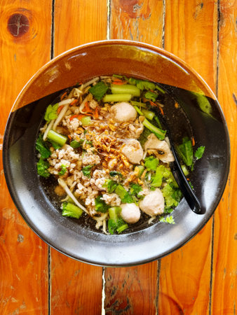 Noodles with meatballs and vegetables in a bowl on wooden table