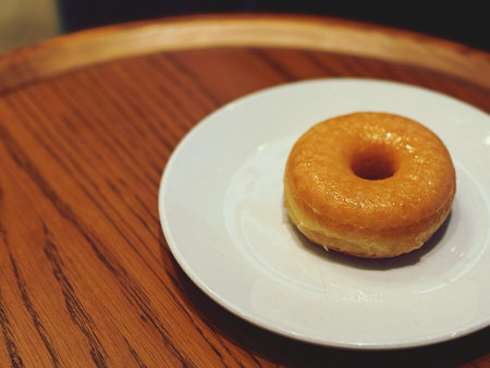 Donut on a white plate on a wooden table. Selective focus.