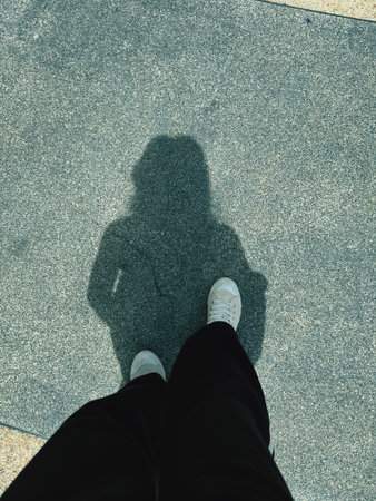 Selfie of person's feet standing on asphalt road with shadow.