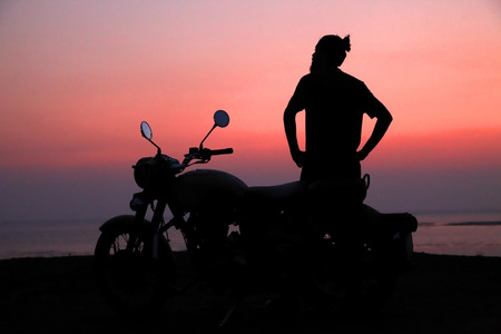 Young man standing near motorbike and enjoying sunset viewの写真素材