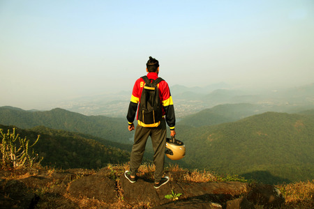 Young man with backpack and helmet standing on the top of a mountain and enjoying valley viewの写真素材