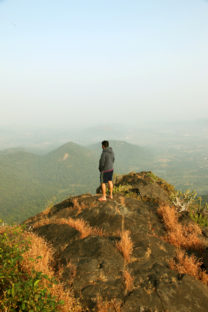 Young man standing on the top of a mountain and enjoying valley viewの写真素材