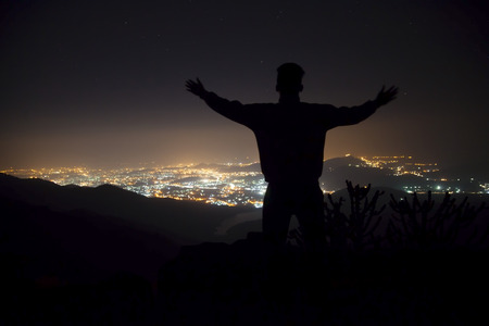 Young man on top of the hill observing the night city view.の写真素材