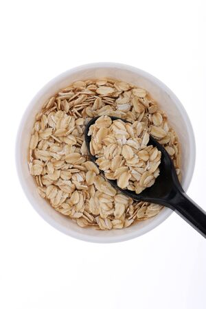 Oat flakes, uncooked oats in bowl with poon and wheat ears on white background. Concept of healthy eating, vegan food, healthy food, breakfast.の写真素材