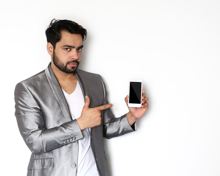 Young indian man pointing at smart phone screen against white background.の写真素材