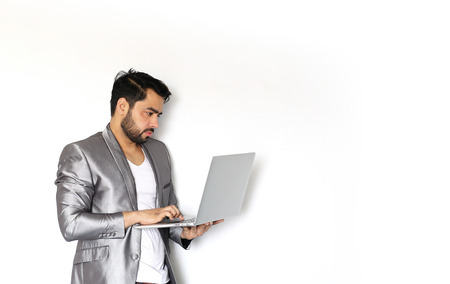 A handsome young Indian man working on laptop against a white backgroundの写真素材