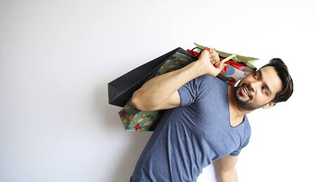 A young Indian man holding shopping bags on white background.