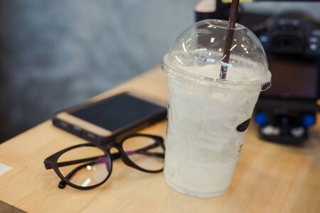 vanilla milk ice in plastic cup with glasses and smart phone on background at cafeの写真素材